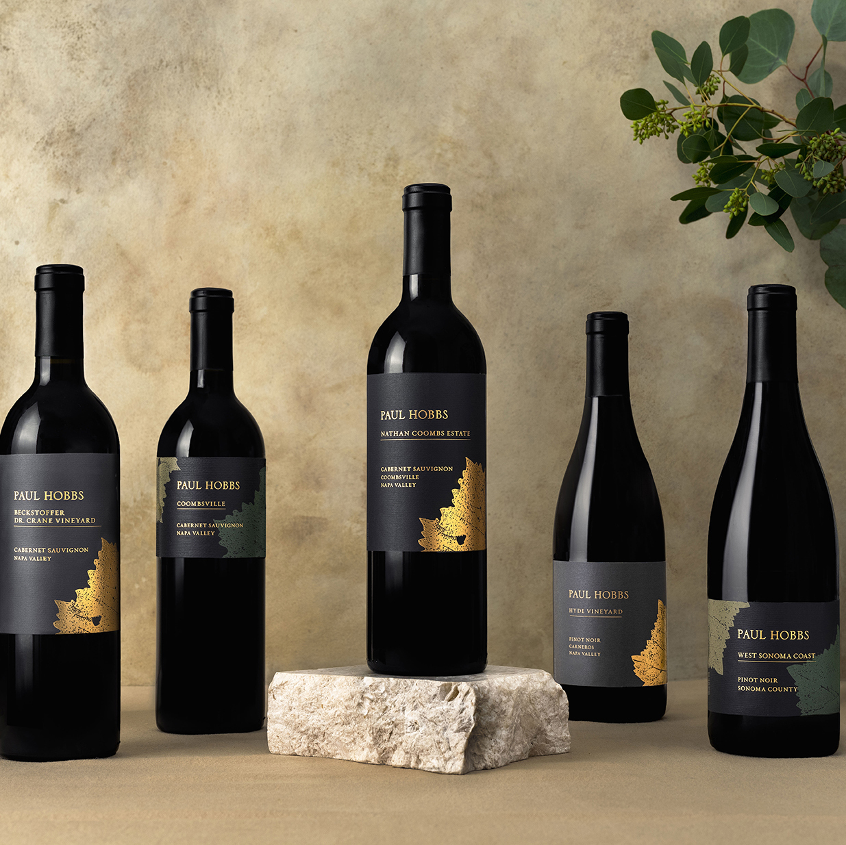 5 wine bottles on a tan linen with eucalyptus in the back right corner